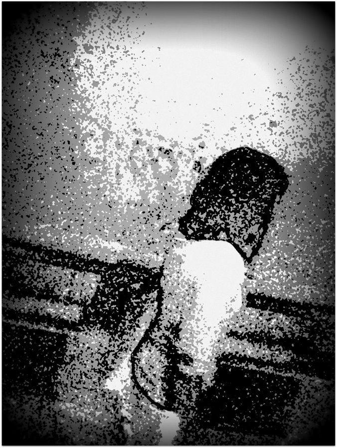 Silhouette assise de dos, dissoute dans un grain noir et blanc très contrasté.